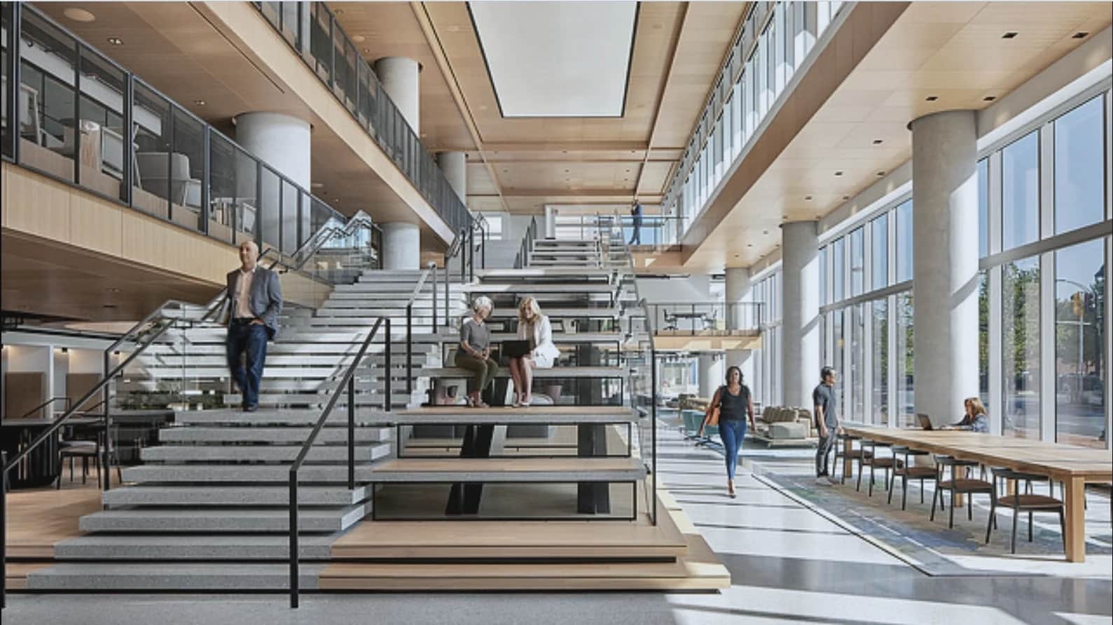 Wide atrium stair with seating steps and black steel handrails in a glass-walled office
