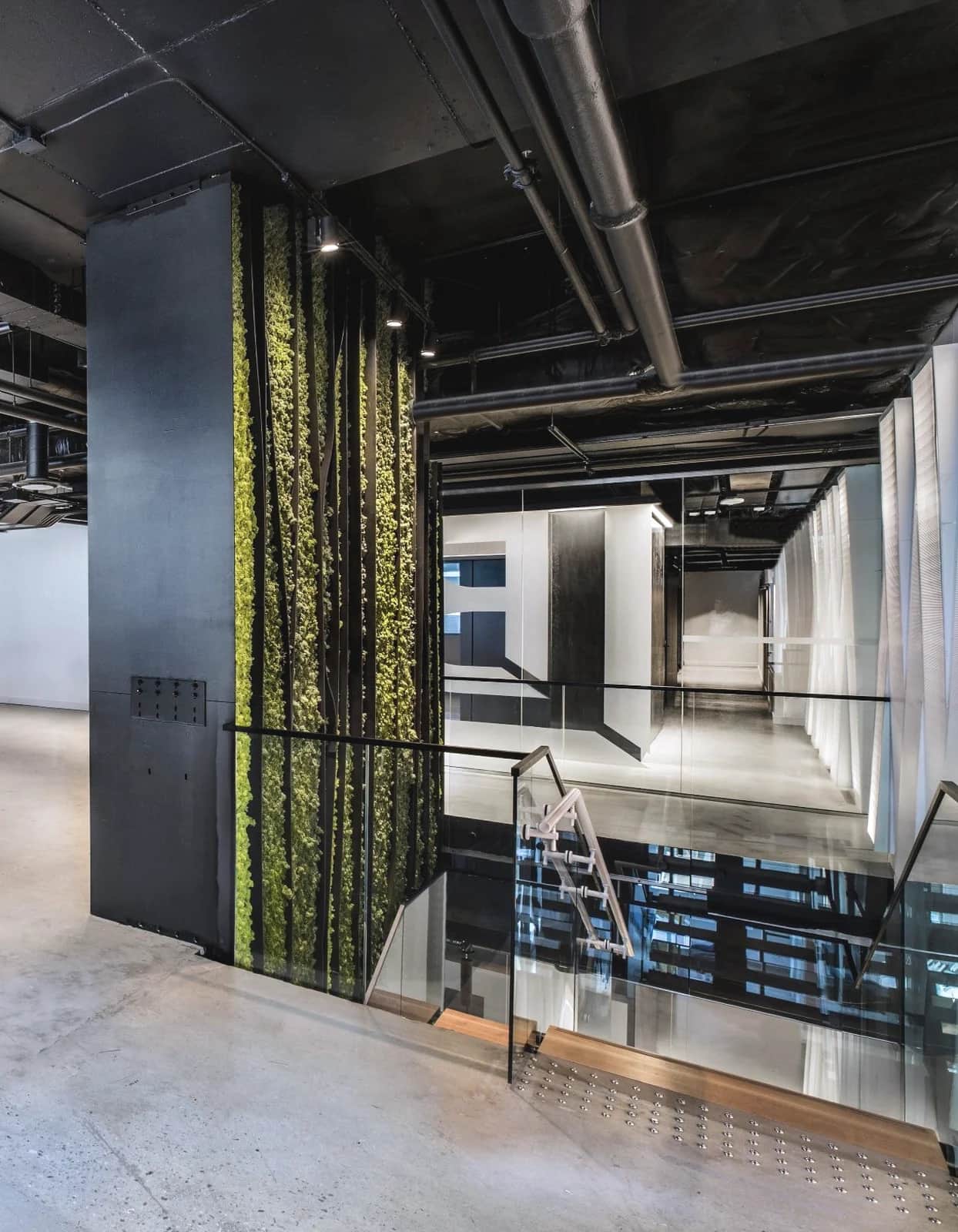 Living-wall stair, Toronto: Glass guardrail around a stair opening beside a living moss wall and a dark steel column
