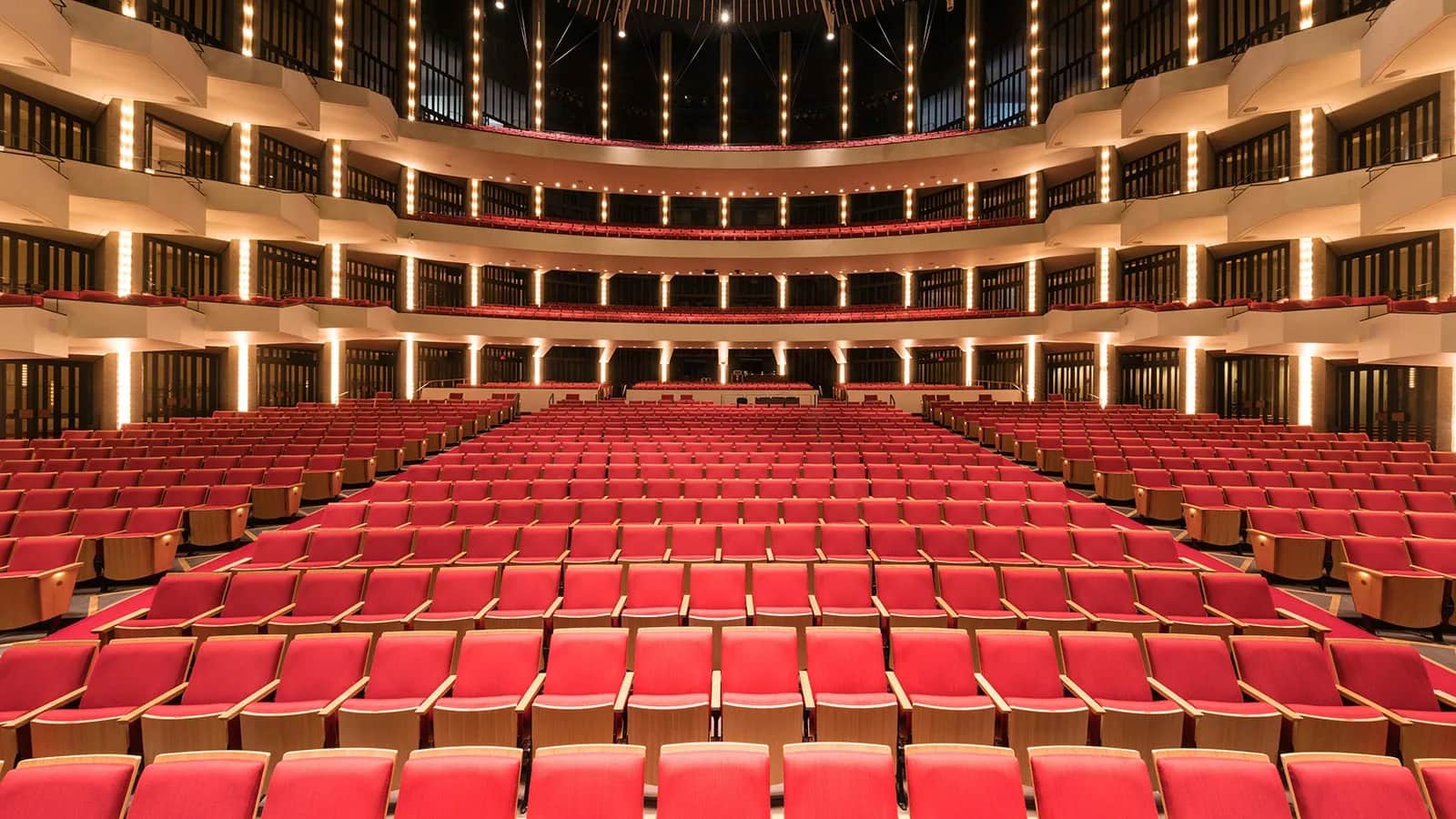 National Arts Centre (NAC), Ottawa: The auditorium seen from the stage: rows of red seats and curved balcony tiers with guardrails, lit by columns of lights
