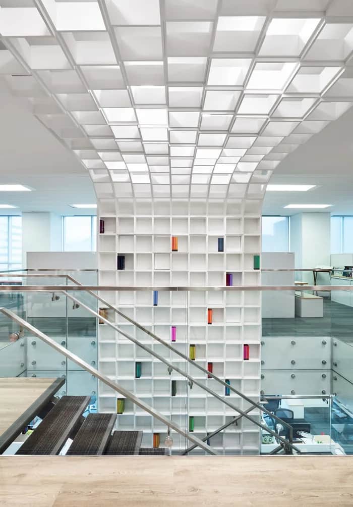 Penguin Stair: Stair with a glass guardrail rising beside a tall wall of white shelving under a coffered ceiling