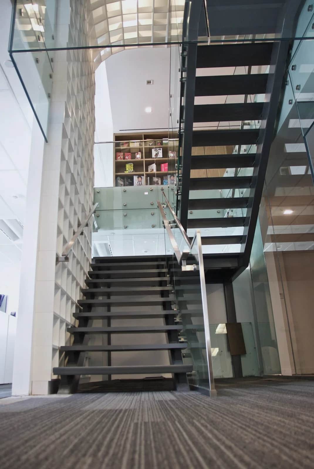 Penguin Stair: Black steel stair with open treads and glass guardrails, seen from the bottom step