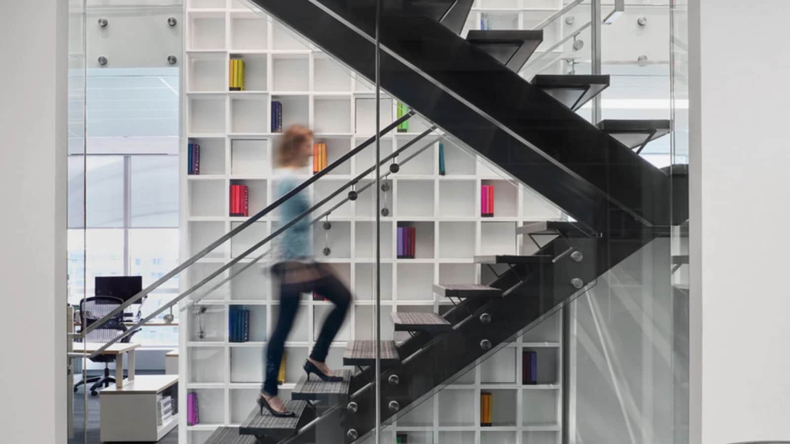 Penguin Stair: Black steel stair with open treads and a glass guardrail in front of white shelving