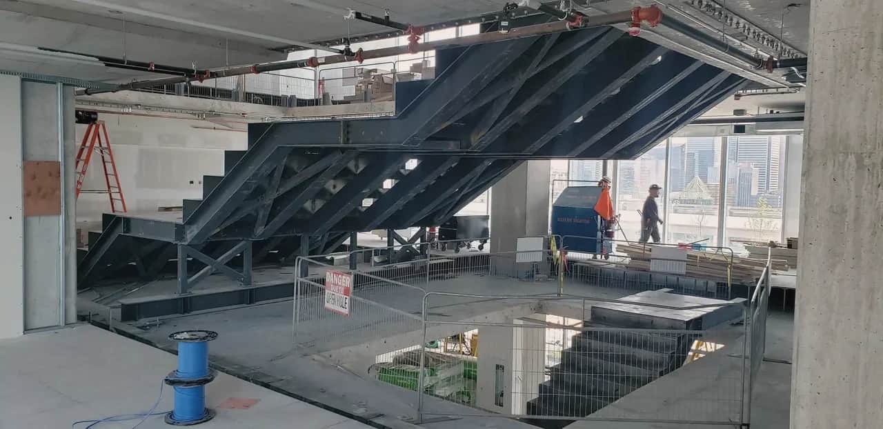 The Well, Toronto: Structural steel stair assembly under construction, with the city skyline through the windows