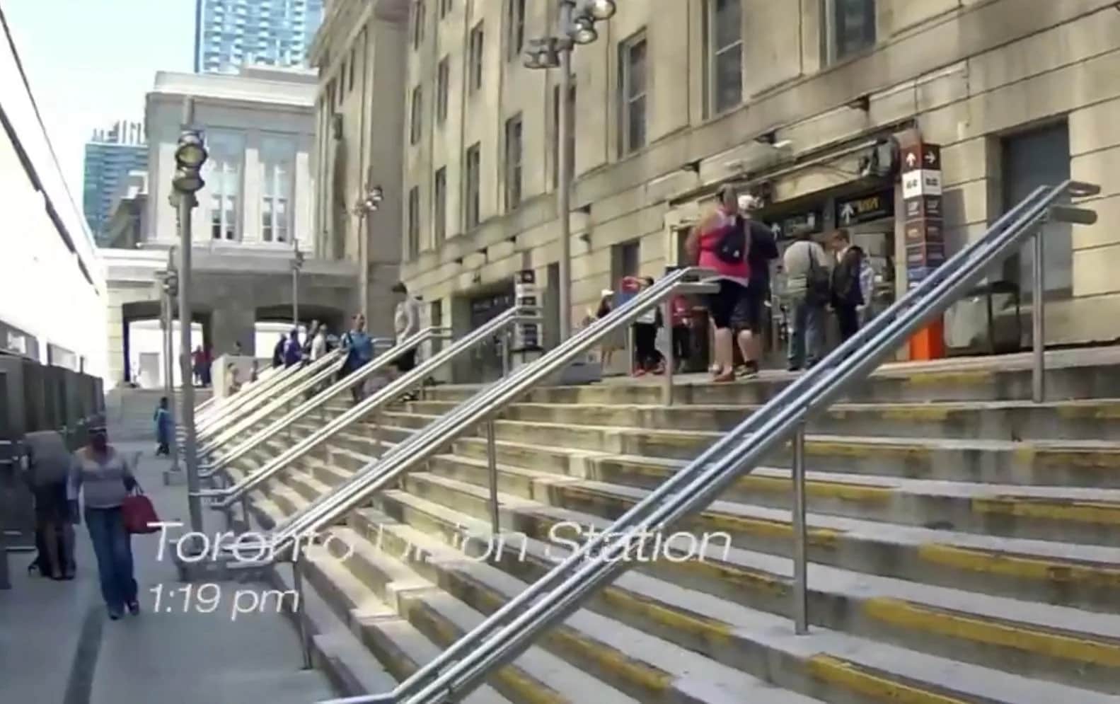 Union Station, Toronto: Video still of a wide exterior stone stair with rows of stainless steel handrails, people on the steps and the station facade beyond, with the burnt-in caption "Toronto Union Station 1:19 pm"