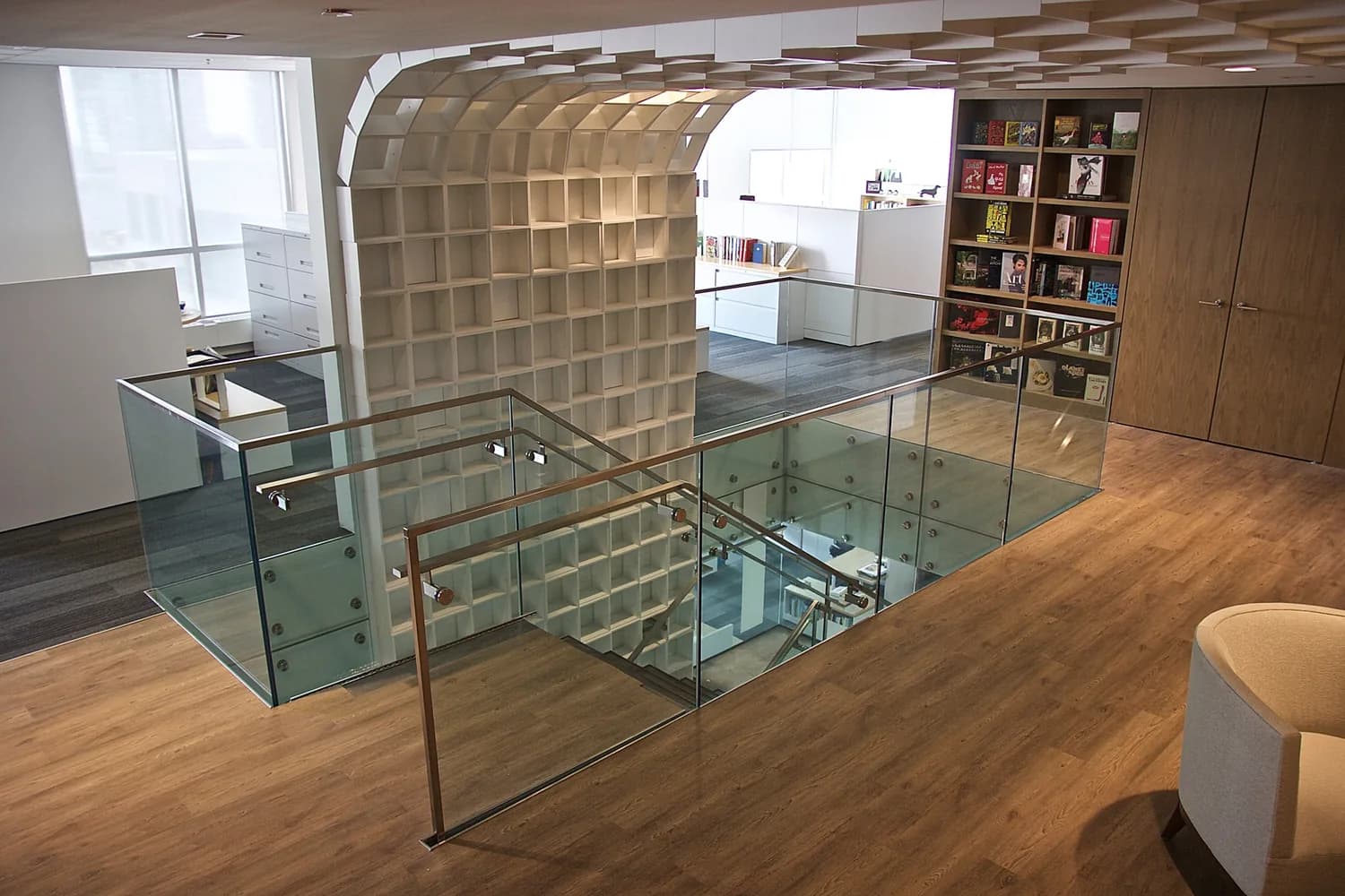 Penguin Stair: Glass guardrail with a stainless steel handrail around a stair opening, next to a curved wall of white shelving