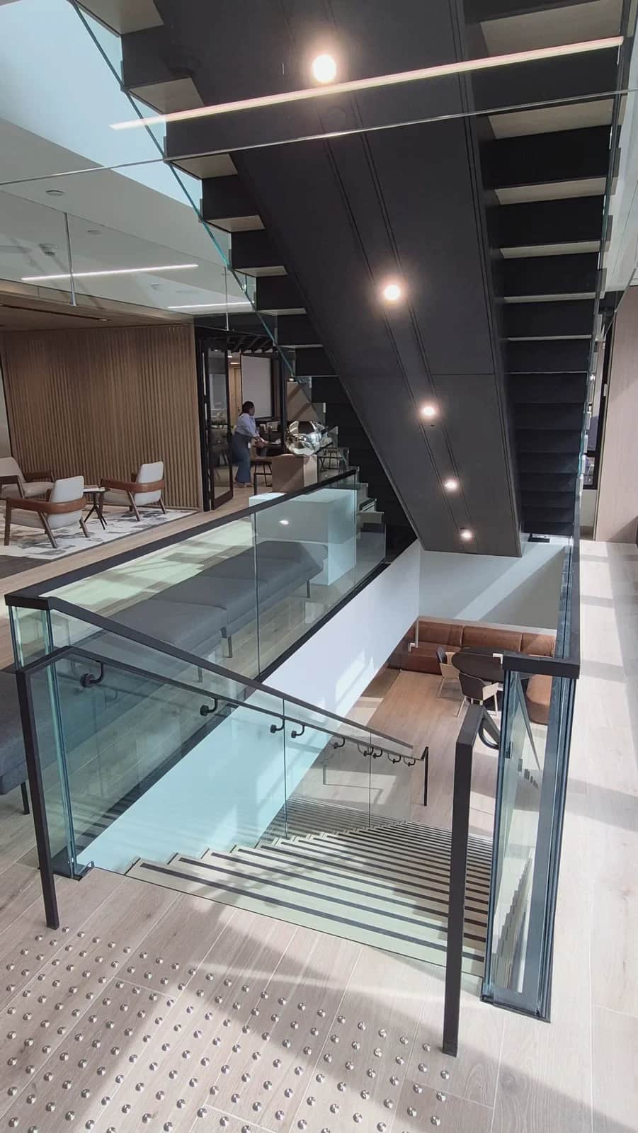 Office staircase, Toronto: Portrait view of the stair opening: the black steel stair above and glass-guarded steps leading down to the floor below